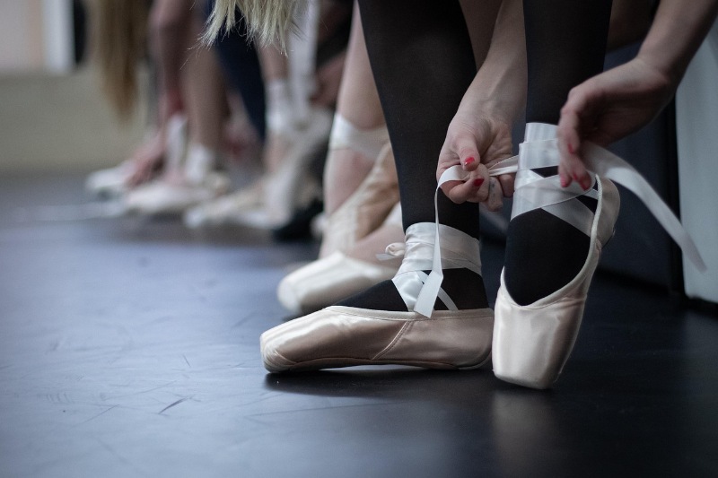 Ballet dancer tying pointe shoes while seated on the floor.