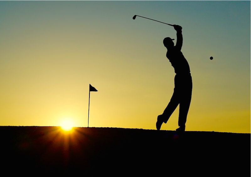 Golfer swinging a club on a green course at Bicester Hotel Golf & Spa.