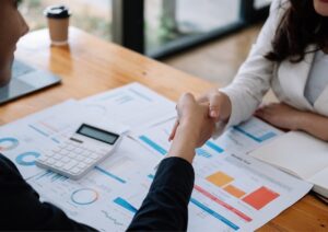 Hands writing notes on paper next to a laptop on an office desk.