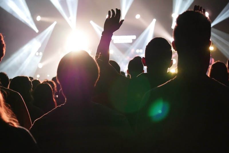 Crowd of people enjoying a live outdoor music festival under bright stage lights.