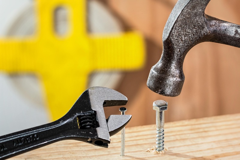 Person hammering a nail into a piece of wood on a workbench.