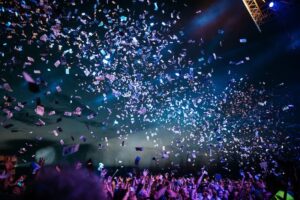 Large crowd enjoying a live music performance under colourful stage lighting.