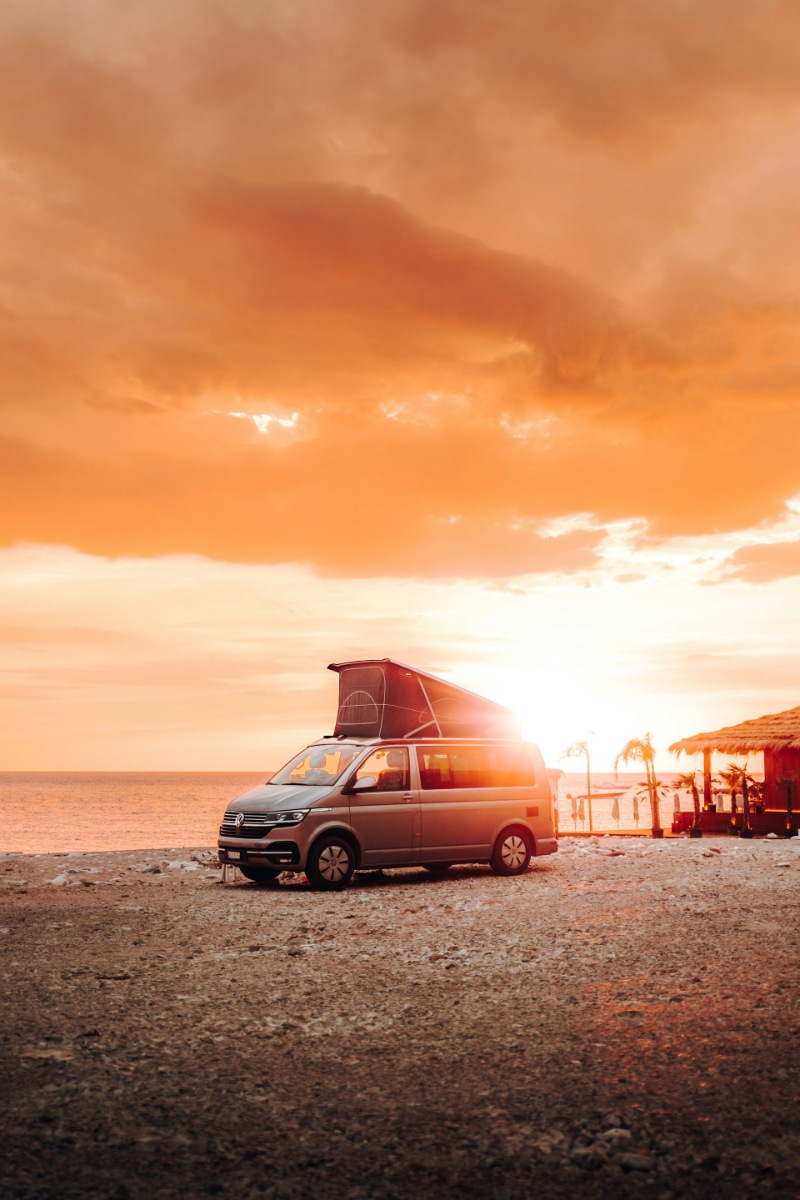 Classic VW campervan parked on a coastal road at sunset.
