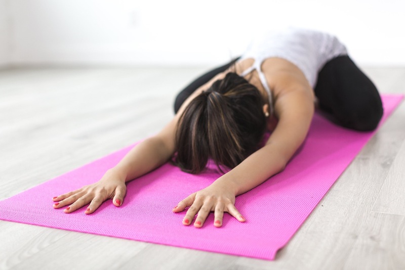 Person practising a yoga pose on a pink mat indoors.