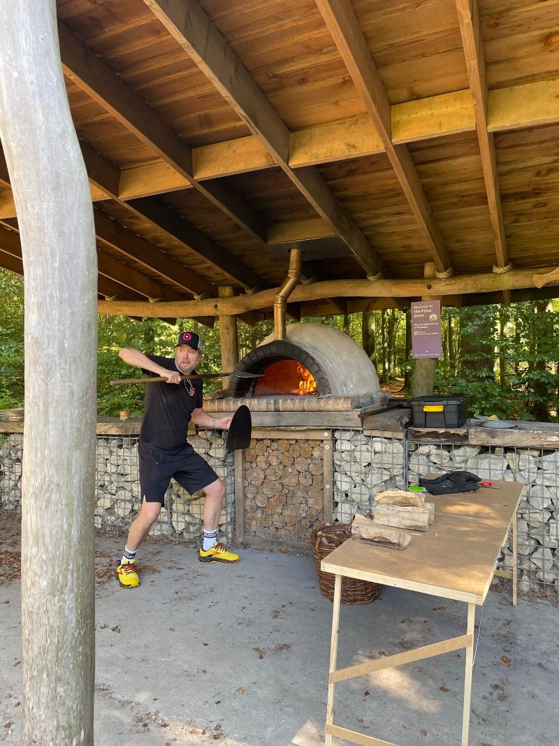 Anders preparing food beside a wood-fired pizza oven.